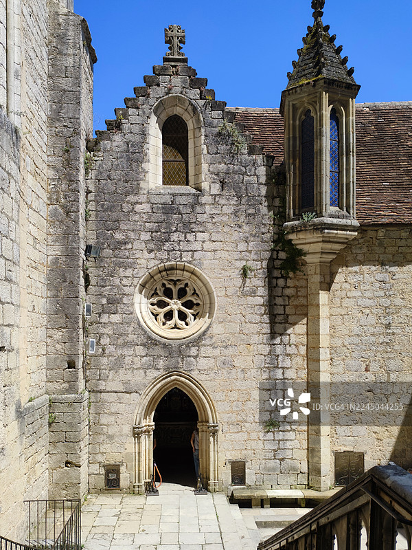 从低角度仰望一座古老的石头教堂，天空湛蓝，突显了哥特式建筑风格和宗教象征意义。地点：Gourdon, France, Rocamadour。图片素材