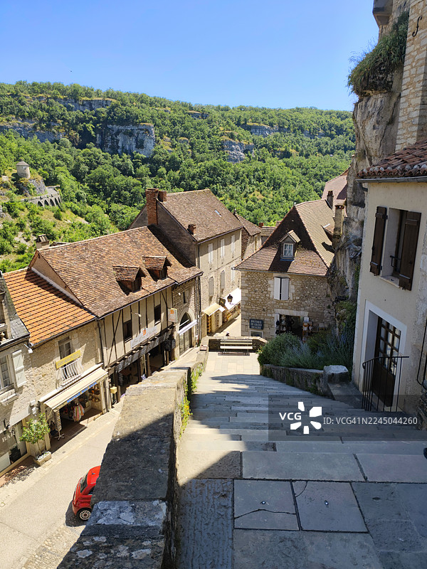 从高处俯瞰法国格尔东（Gourdon）村庄，蜿蜒的街道两旁是历史建筑，背景是郁郁葱葱的绿色山丘。也可能是法国的罗卡马杜尔（Rocamadour）。图片素材