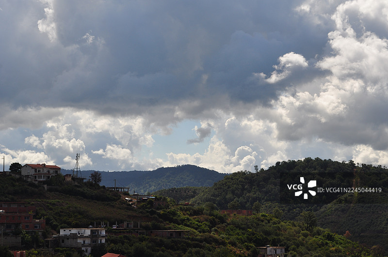 戏剧性多云天空下，坐落在绿色山丘中的城镇全景图片素材