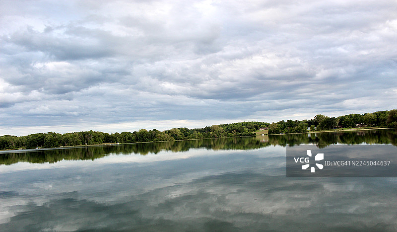 宁静的湖泊倒映着多云的天空和远处岸边郁郁葱葱的绿树，构成一幅宁静的自然风光，美国韦斯特菲尔德图片素材