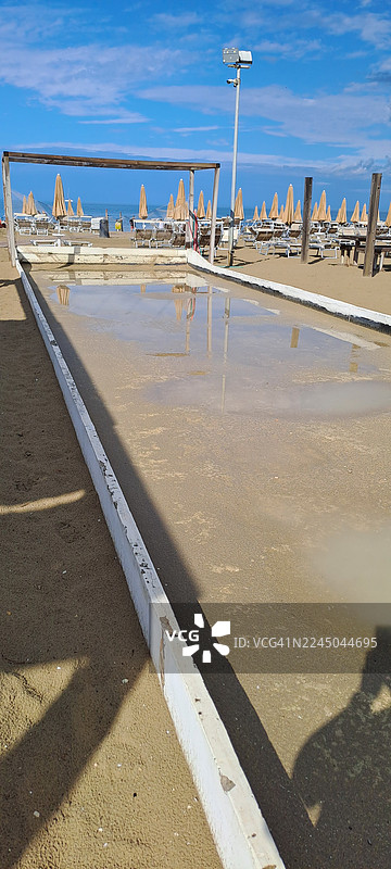 意大利里米尼里瓦贝拉海滩上的 bocce 球场，背景为大海，带有遮阳伞，天空湛蓝图片素材