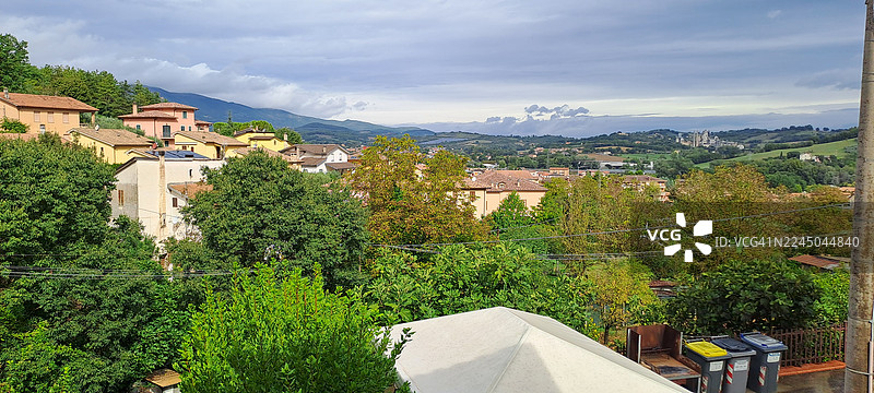 俯瞰风光如画的意大利小镇，坐落于山谷之中，四周绿树成荫，远方是连绵的山峦，天空布满云彩。图片素材