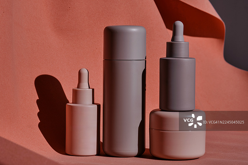 柔和中性色调的各种化妆品瓶罐的特写工作室拍摄，摆放在带有自然光影的纹理表面上图片素材
