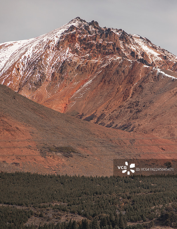 阿根廷埃斯克尔，白雪皑皑的雄伟山峰，崎岖的地形，下方是茂密的森林，天空多云图片素材