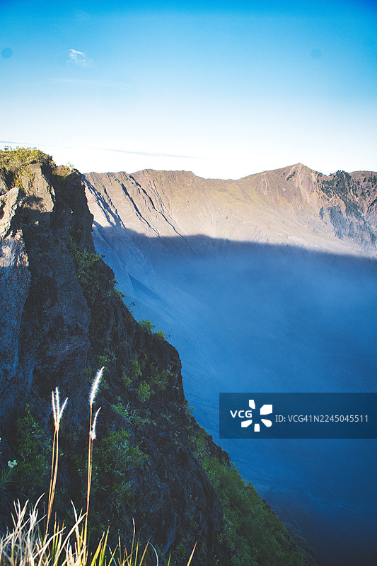 印尼松巴哇巴拉特，晴朗蓝天下，深邃的山谷被薄雾笼罩，壮丽的山景图片素材