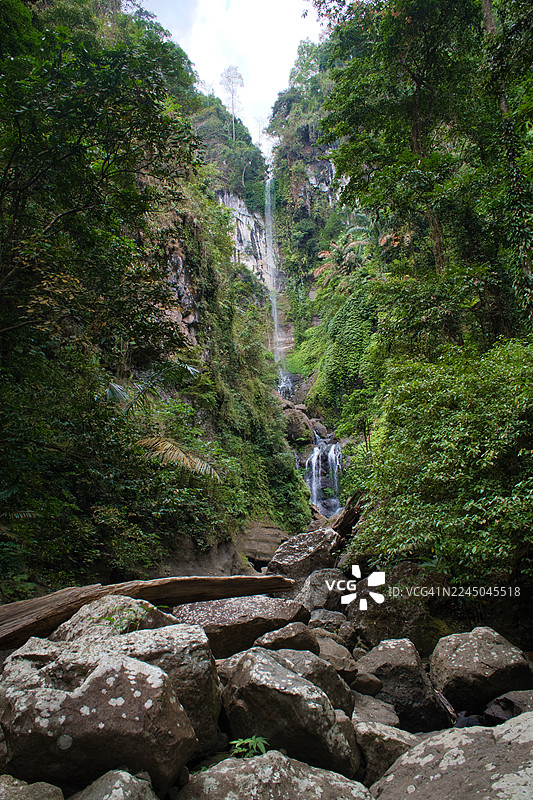 印尼松巴哇巴拉特，郁郁葱葱的热带雨林中，雄伟的瀑布飞流直下，周围岩石青翠。图片素材