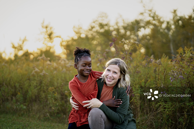 阳光明媚的野花田中，快乐的黑人女孩和白人女性拥抱在一起图片素材
