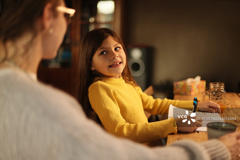 小女孩在做作业时，微笑着看着她的母亲。图片素材
