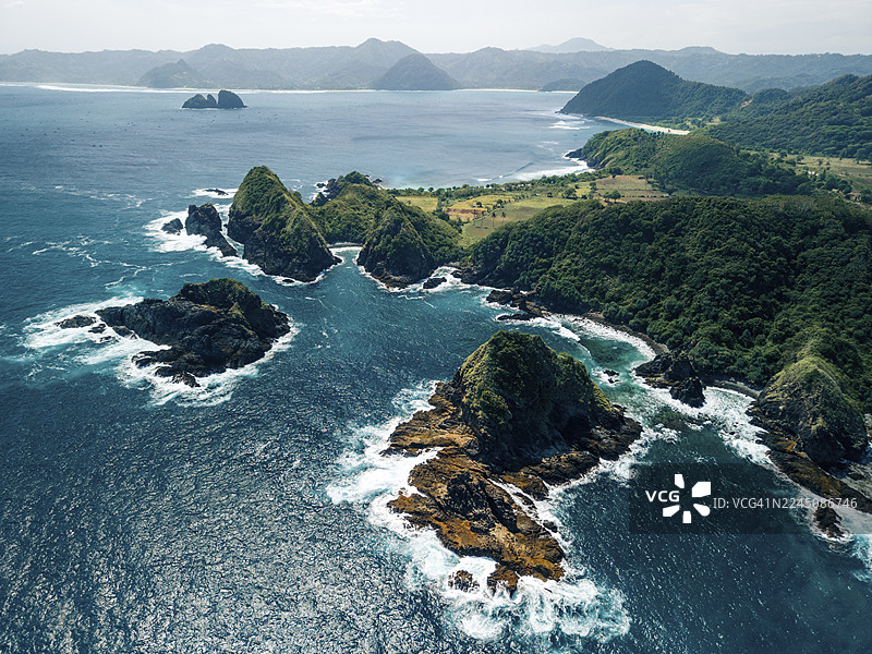 从空中俯瞰崎岖的海岸线，郁郁葱葱的绿色山丘和深蓝色的大海拍打着岩石。印度尼西亚，努沙登加拉巴鲁，格鲁普克海滩，布洛姆海滩。图片素材