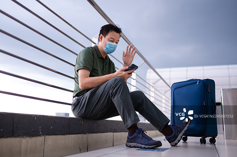 一名戴着防护口罩的亚洲男性旅行者在机场航站楼用智能手机与家人进行视频通话图片素材