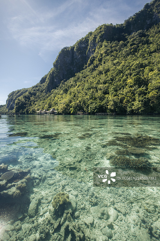 碧绿山峦下的水晶般清澈的海水与珊瑚礁，配以蓝天。印度尼西亚马鲁古省塞尔姆岛萨莱曼村。图片素材