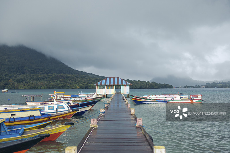背景是山脉和多云的天空，色彩斑斓的船只停靠在码头。印度尼西亚，马鲁古省中部，班达，班达内拉图片素材