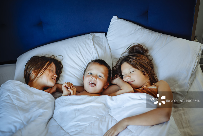 亲密无间——三个孩子在卧室温馨的晨光中共处图片素材