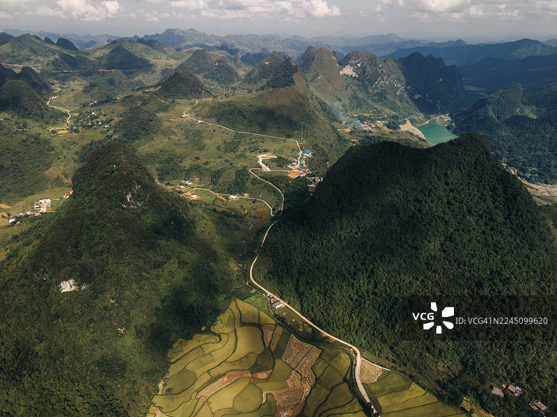 越南高平省阮平县，蓝天下的葱郁青山、蜿蜒道路和梯田的航拍景象图片素材