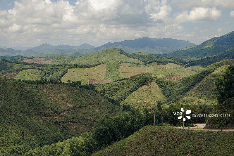越南北江省山洞县，部分多云的天空下连绵的绿色山丘，远方地平线上有山脉。图片素材