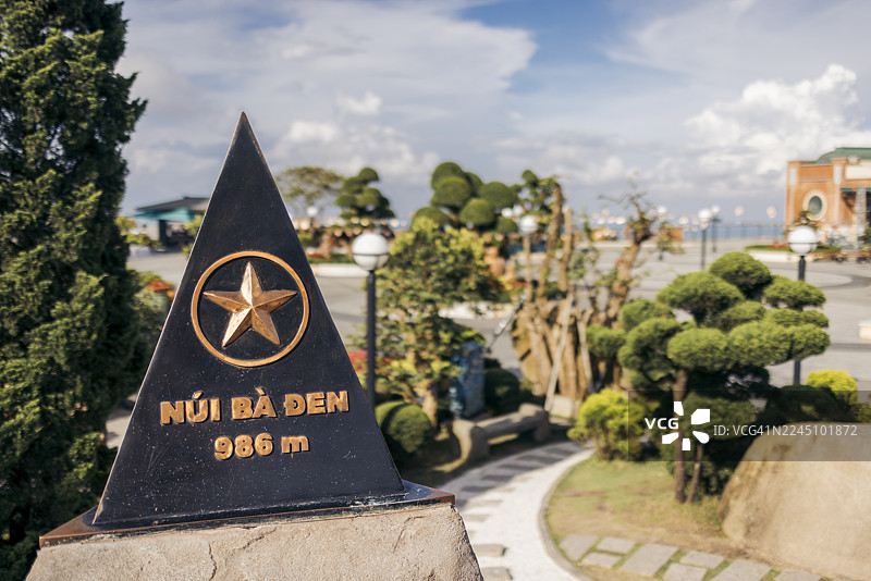 阳光明媚的日子里，一座石碑矗立着，远眺着精心打理的树木和远处的建筑。越南茶宁省黑女士山。图片素材