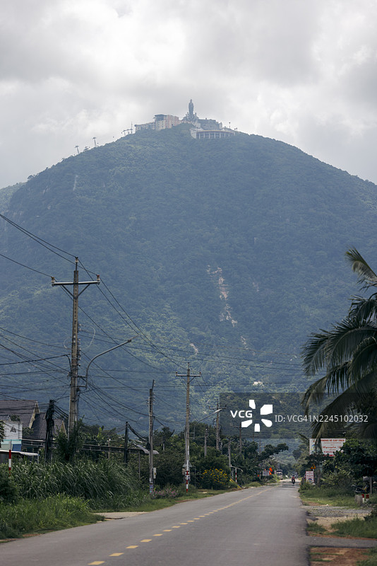 一条路通向山顶的雕像，周围环绕着云彩和茂密的绿植。越南茶宁省黑娘山。图片素材