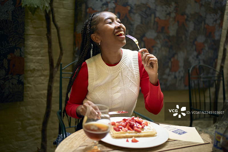 一位女士在咖啡馆的桌子旁，开心地享用着华夫饼和新鲜草莓。地点：比利时布鲁日。图片素材