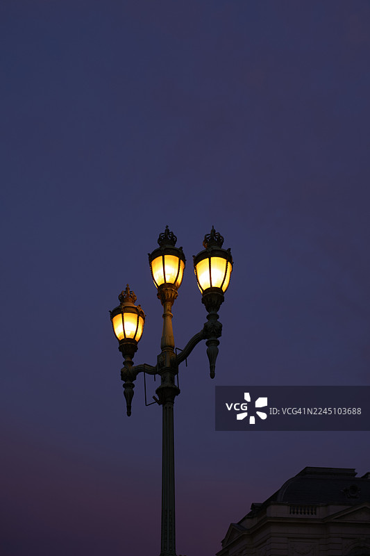 深邃的暮色天空背景下，三盏复古的路灯散发出温暖的光芒。比利时西弗兰德省布兰肯贝赫。图片素材