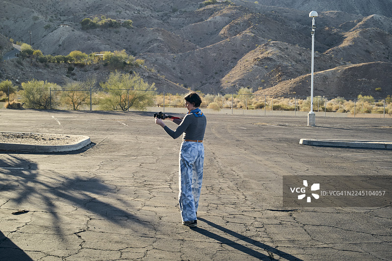 年轻女子在荒凉的停车场拍摄，周围是干旱的山地景观。美国加利福尼亚州图片素材
