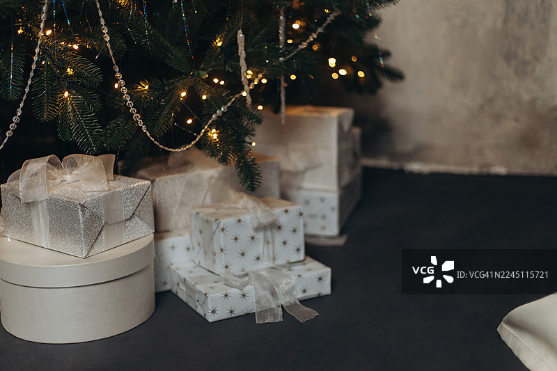 白色和银色的包装礼盒摆放在华丽的圣诞树下，树上装饰着彩灯和珠串饰品。图片素材