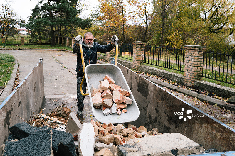 一名建筑工人将手推车中的砖块倒入运输集装箱图片素材
