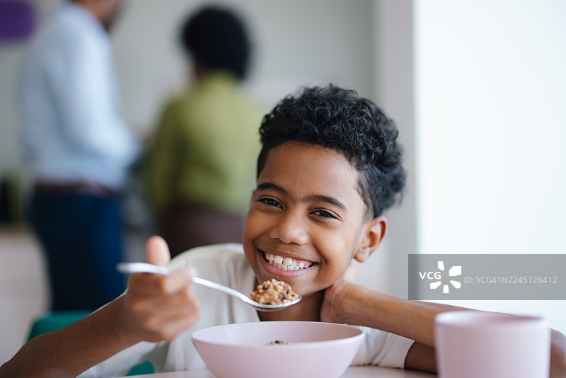 微笑的孩子在家享受早餐，手持碗和勺子的快乐早晨时光图片素材