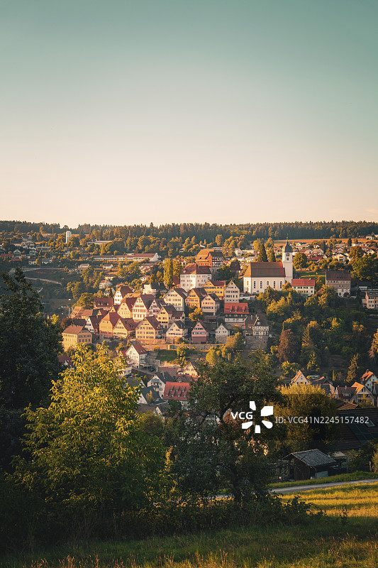 德国卡尔夫区阿尔滕施泰格村庄在山丘上的教堂景色，温暖的阳光透过树林闪耀图片素材