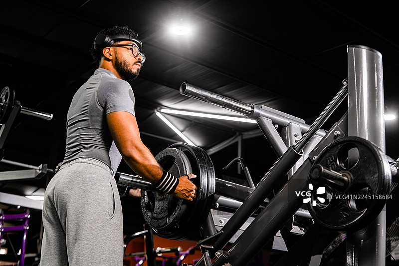 健壮的男人在健身器材上加负重进行力量训练图片素材