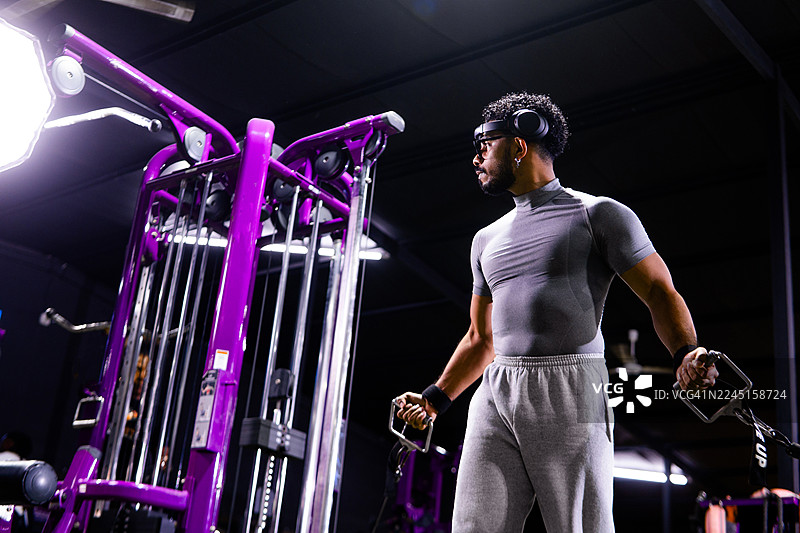 现代健身房里，一名男子正在使用力量训练器械锻炼图片素材