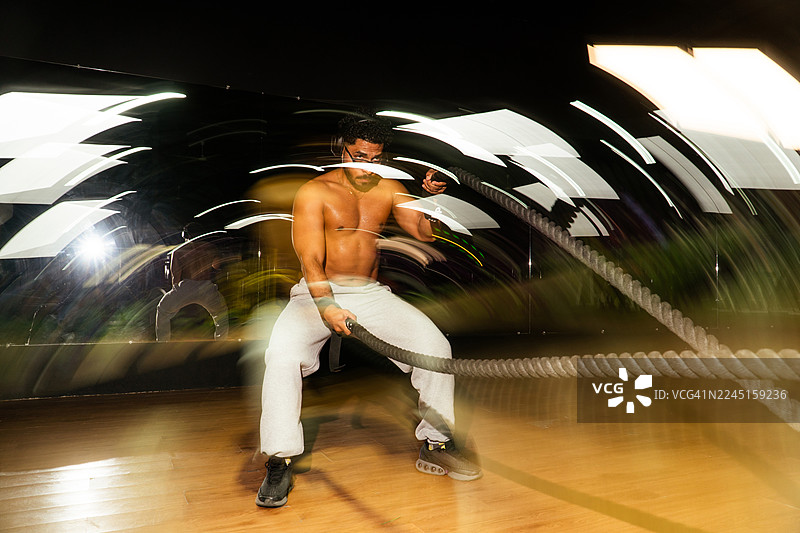 专注的男人正在挥舞战绳进行训练，背景有动态模糊效果图片素材