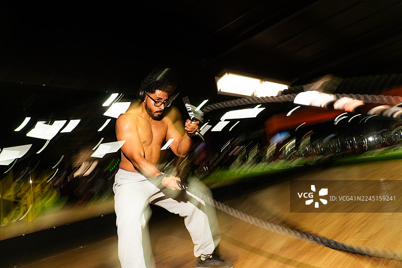 健身房里，一个男人正在挥舞战绳进行锻炼，画面有运动模糊效果图片素材