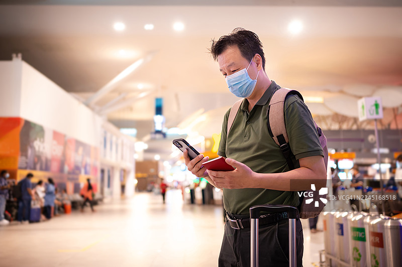 一名戴着防护口罩的亚洲男性旅客正在查看智能手机上的出发时间图片素材