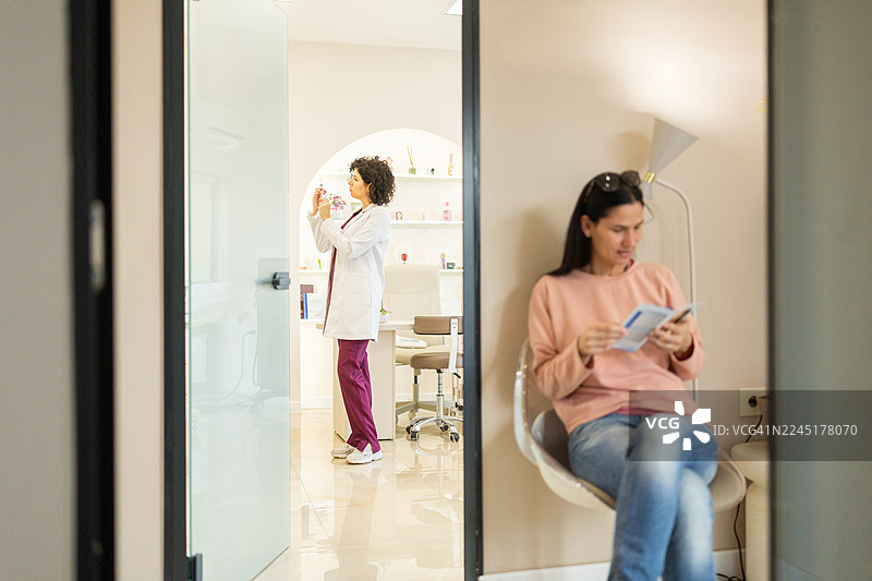 女子在现代诊所候诊室等待，医生在背景中进行检查图片素材
