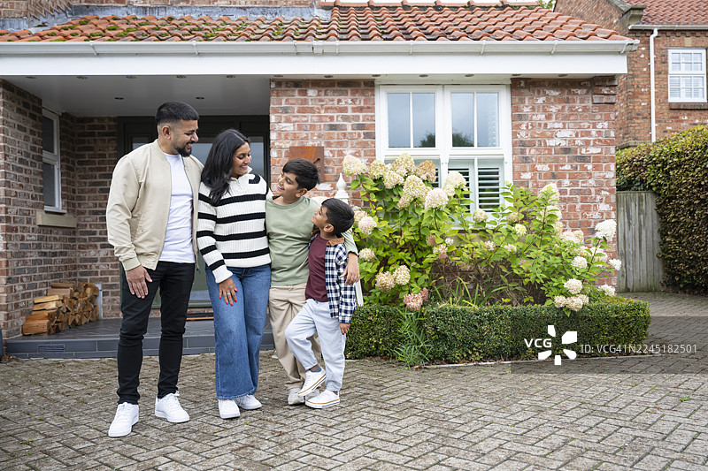 一对英籍巴基斯坦夫妇带着两个孩子，站在一栋现代郊区别墅外图片素材