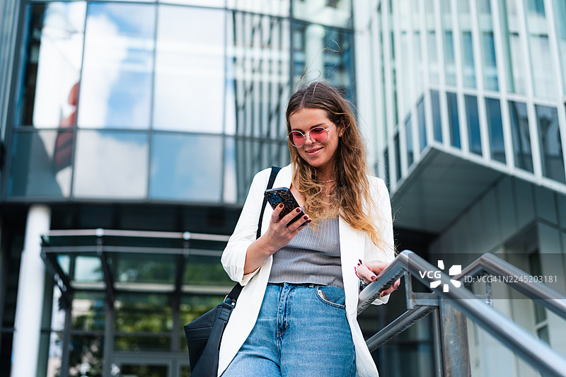 年轻女子在城市商业区户外愉快地使用智能手机图片素材