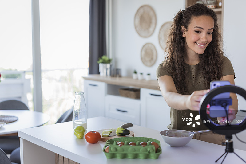 一位女性使用智能手机和补光灯拍摄烹饪视频图片素材