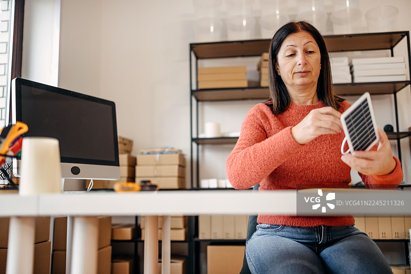 一位女性坐在小型家庭仓库里，进行在线销售和打包图片素材