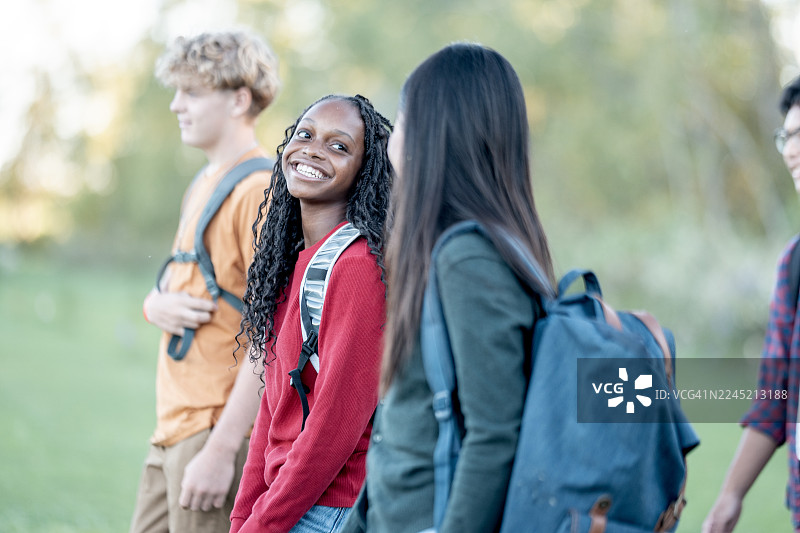 一群快乐的多元化学生背着背包，面带微笑地在校园公园里散步图片素材