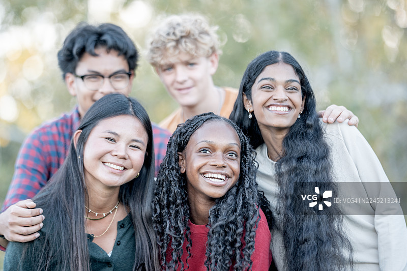 一群多元化的朋友在阳光明媚的公园里，脸上带着笑容，合影留念图片素材