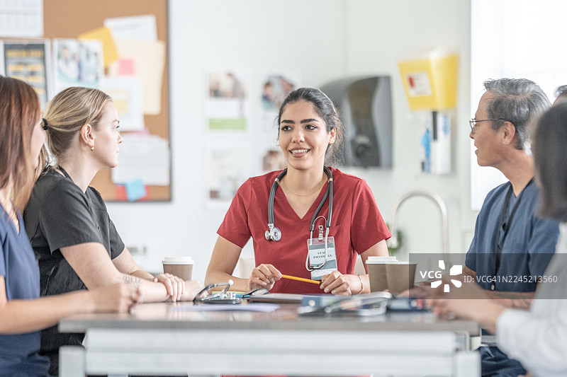 医生们在会议上围坐在诊所的桌子旁，讨论着病人的护理，桌上放着听诊器和病历。图片素材