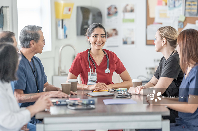 多元化的医疗团队在诊所围坐在桌旁开会，讨论患者护理事宜图片素材