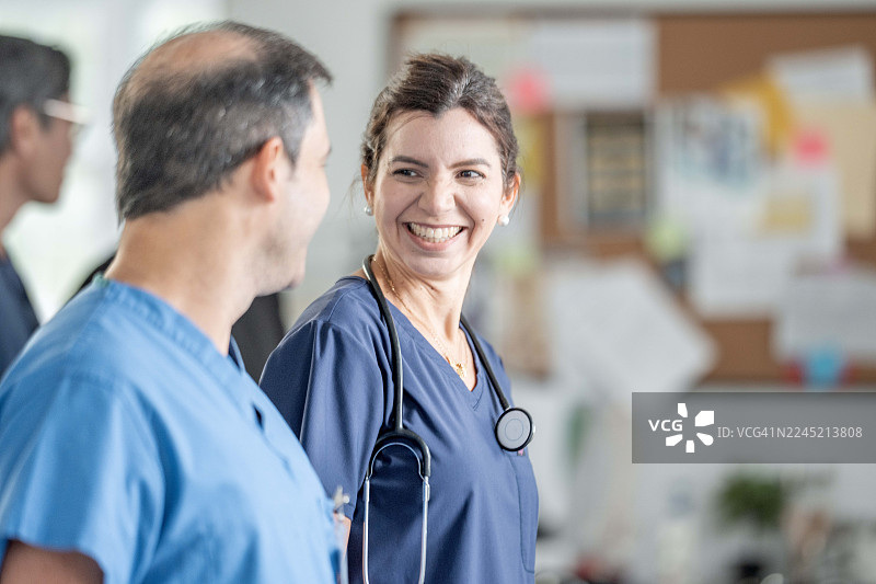 一位戴着听诊器的微笑女护士在明亮的医院走廊里与同事交谈图片素材