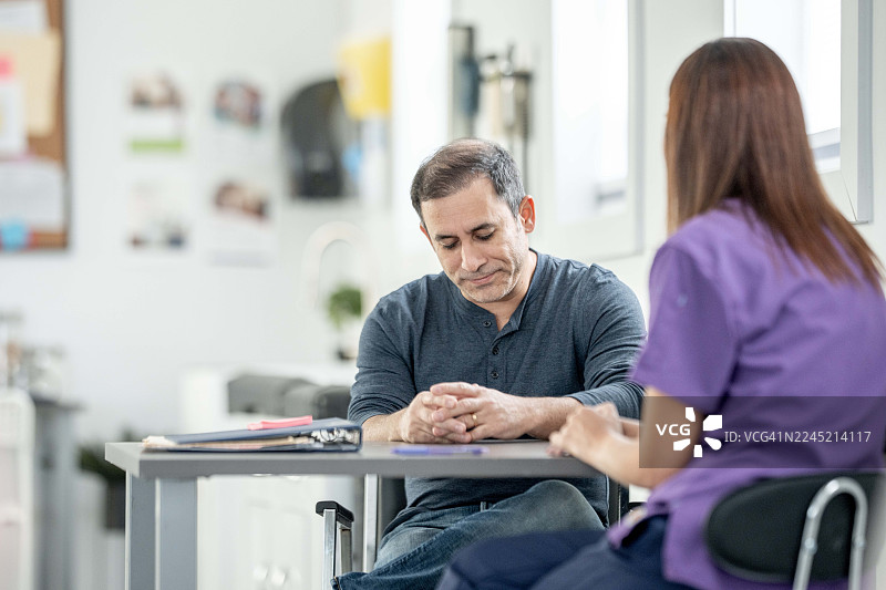 男性成年患者在就诊时，在诊室办公桌前咨询女性护士图片素材