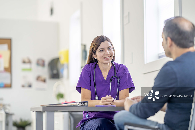身穿紫色护士服的女性护士在明亮的诊室里咨询男性病人图片素材
