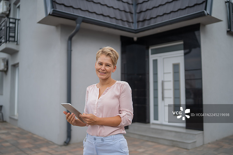 女房地产经纪人手持平板电脑站在房屋前图片素材