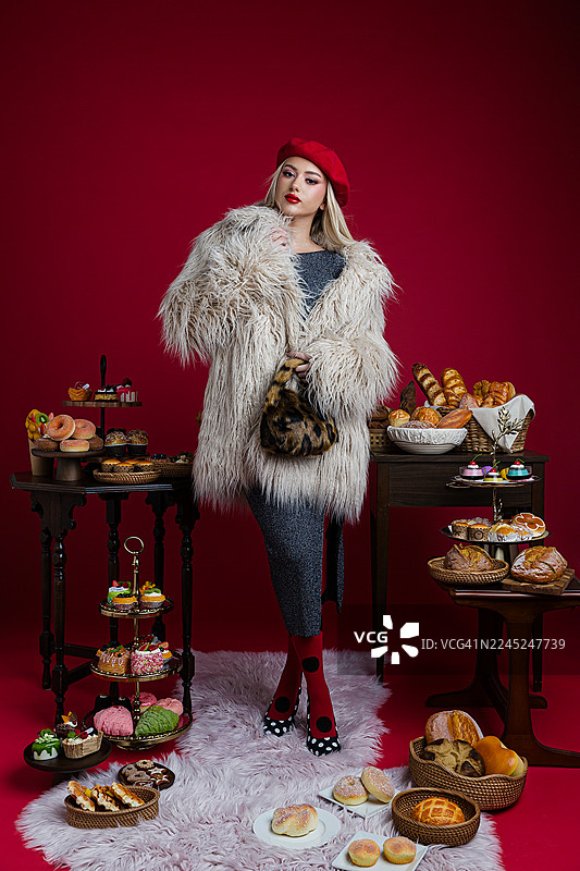 身穿仿皮草外套的时尚女性，手持甜点和糕点摆拍图片素材