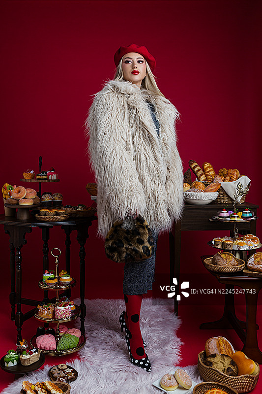 穿着人造毛皮大衣的时髦女子，摆姿势展示甜点和糕点图片素材