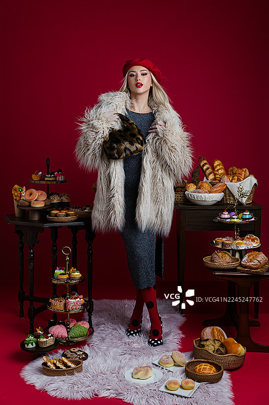 穿着仿皮草大衣的时尚女子，手持甜点和糕点摆姿势图片素材