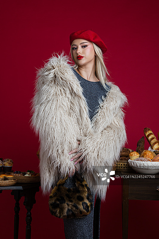 穿着人造毛皮大衣的时髦女子摆姿势，旁边放着甜点和糕点图片素材
